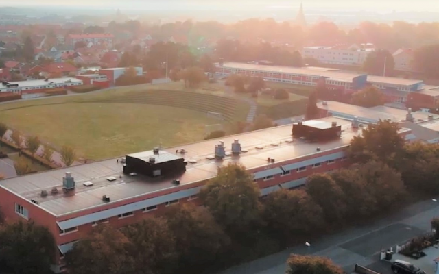 Bild tagen ovanifrån från luften på en skola med en stor gräsplan och en parkering